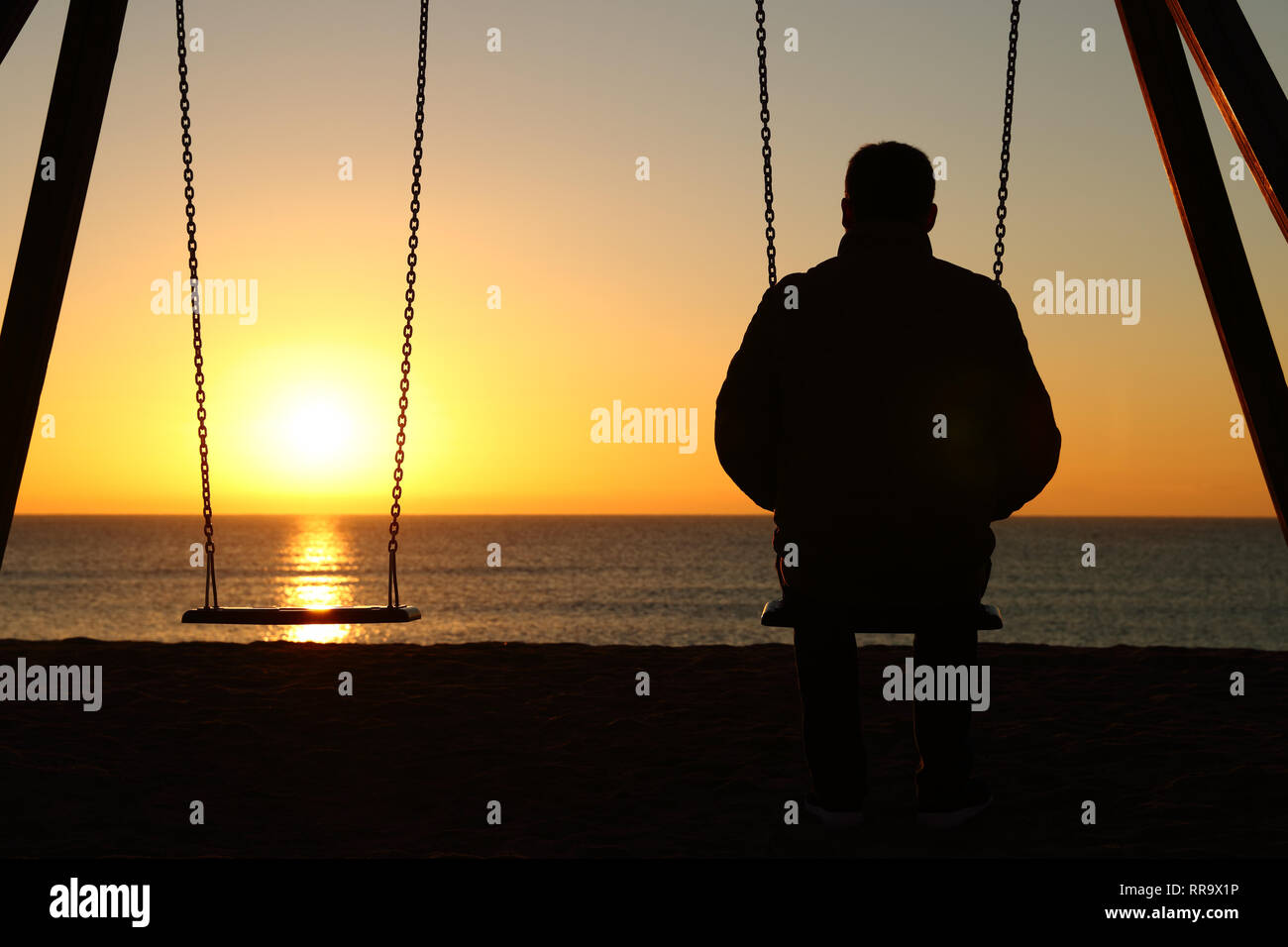 Rétroéclairage vue arrière silhouette d'un homme assis sur la balançoire à elle seule au coucher du soleil sur la plage Banque D'Images