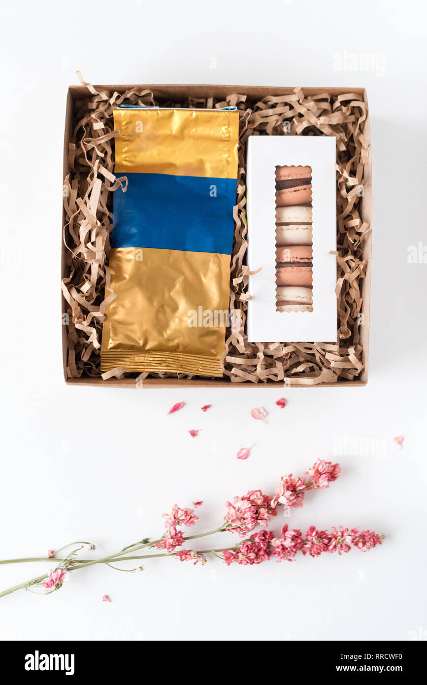 Macarons français avec pack de café en papier craft marron boîte-cadeau. Macarons sucrés en boîte et fleurs séchées sur tableau blanc. Haut de la vue, télévision lay. Banque D'Images