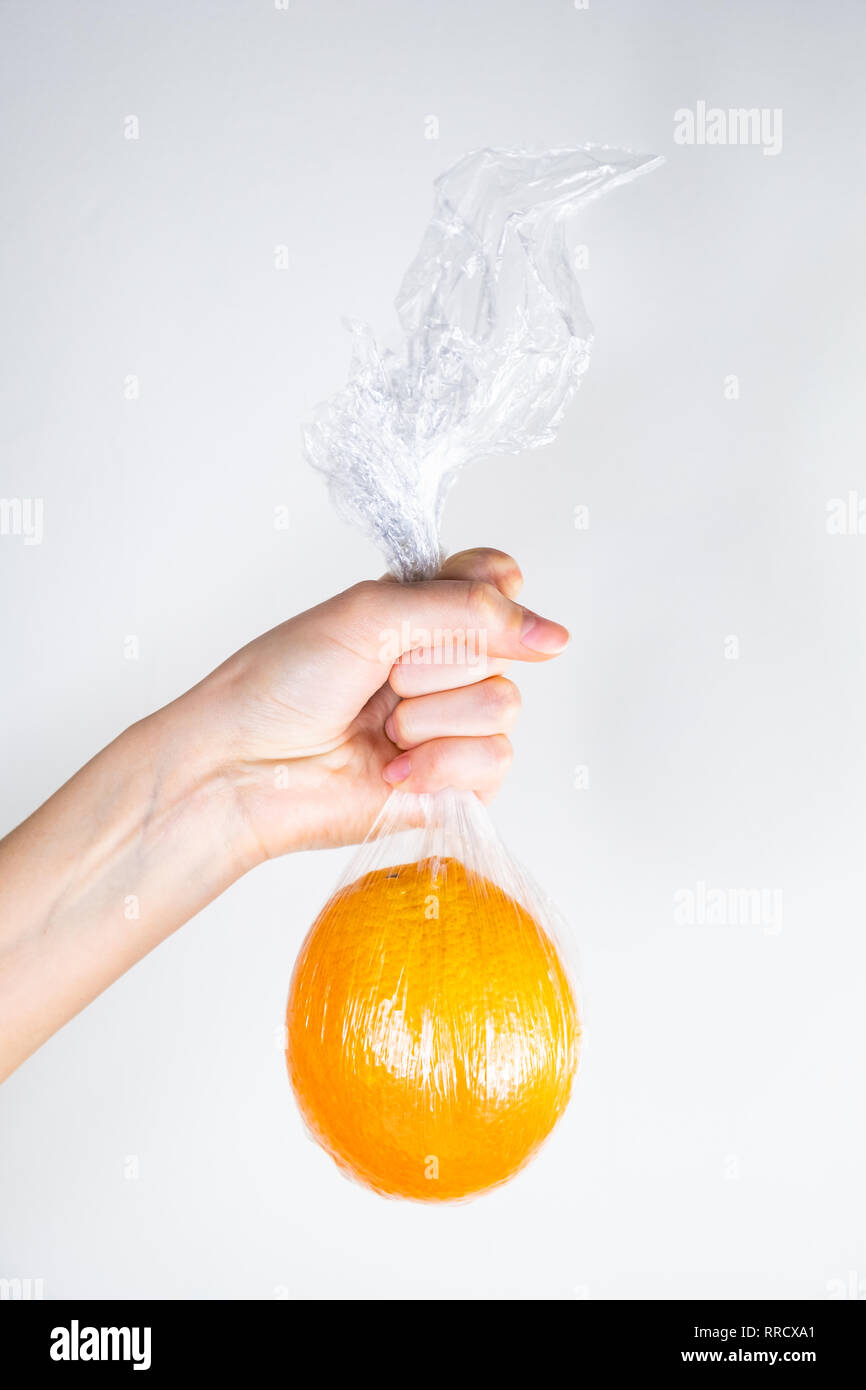 Concept d'utilisation de plastique excessive : orange en plastique qui s'est tenue à une main. Plus injustifié des produits alimentaires préemballés : personne détient des fruits dans la cuisine wr Banque D'Images