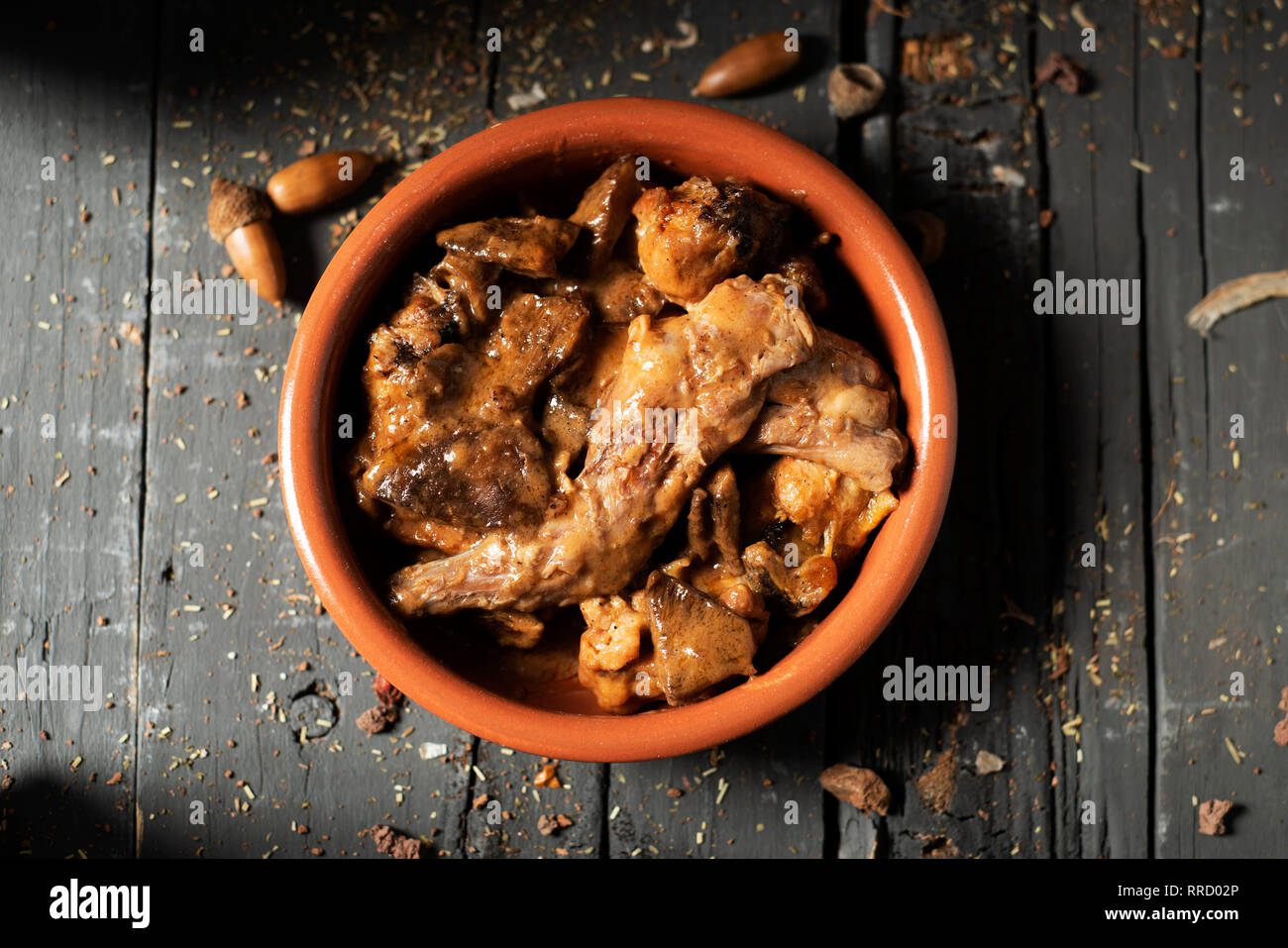 Portrait d'une cocotte en terre cuite avec quelques morceaux de lapin, les pruneaux et les champignons, généralement consommé en Espagne, sur une table en bois rustique gris Banque D'Images