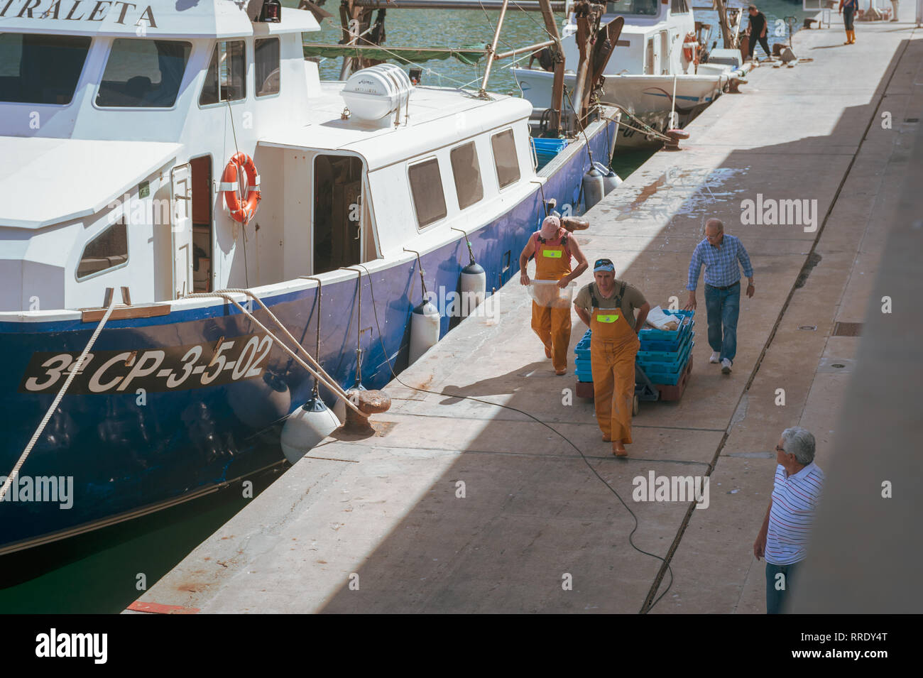Les pêcheurs se promènent un chariot de boîtes contenant du poisson frais, récemment déchargé d'un bateau de pêche, le long du quai au port de Denia en Espagne. Banque D'Images