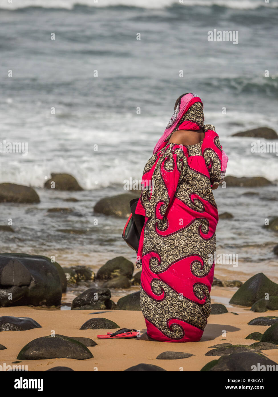 Une figure d'une femme musulmane dans un boubou rouge priant au rivage de l'océan. Le Sénégal. L'Afrique. Banque D'Images