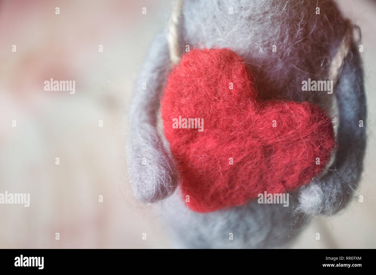 Souris jouet fait de laine entre les mains d'un gros cœur rouge Banque D'Images