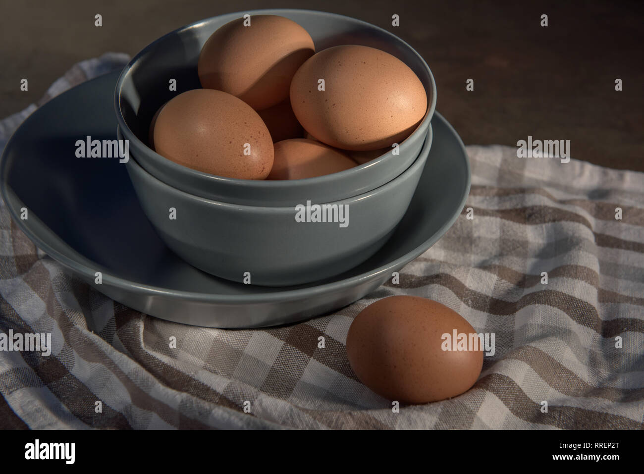 Les oeufs de poule dans un bol gris sur une serviette à carreaux. Banque D'Images