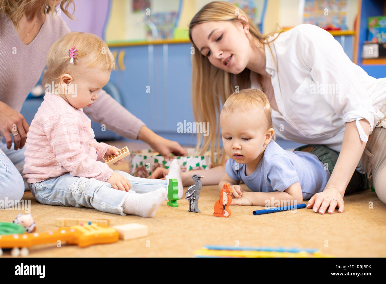 Les bébés de pépinière avec des mamans ou des enseignants à jouer avec des jouets éducatifs en bois assis sur un étage Piscine Banque D'Images
