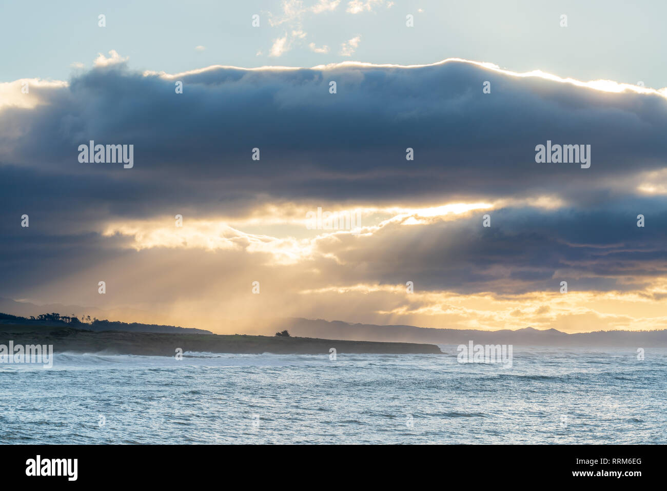 Nuages part lors d'un lever de soleil sur la côte de Californie. Créer de beaux rayons de lumière à travers l'ocean spray près de Cambria. Banque D'Images
