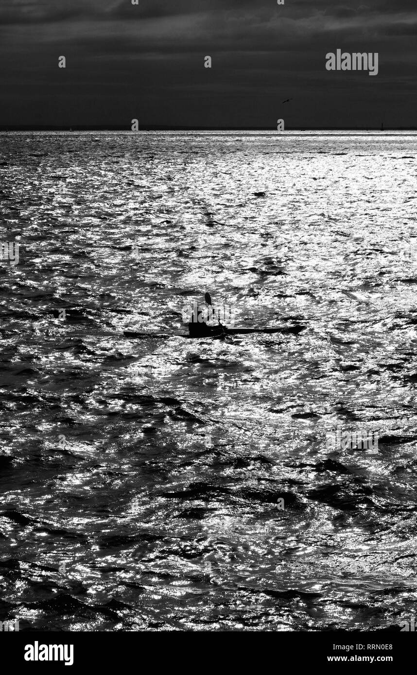 L'homme rendez-vous sur un kayak le long de la baie dans le reflet de reflet du soleil sur l'eau. Banque D'Images