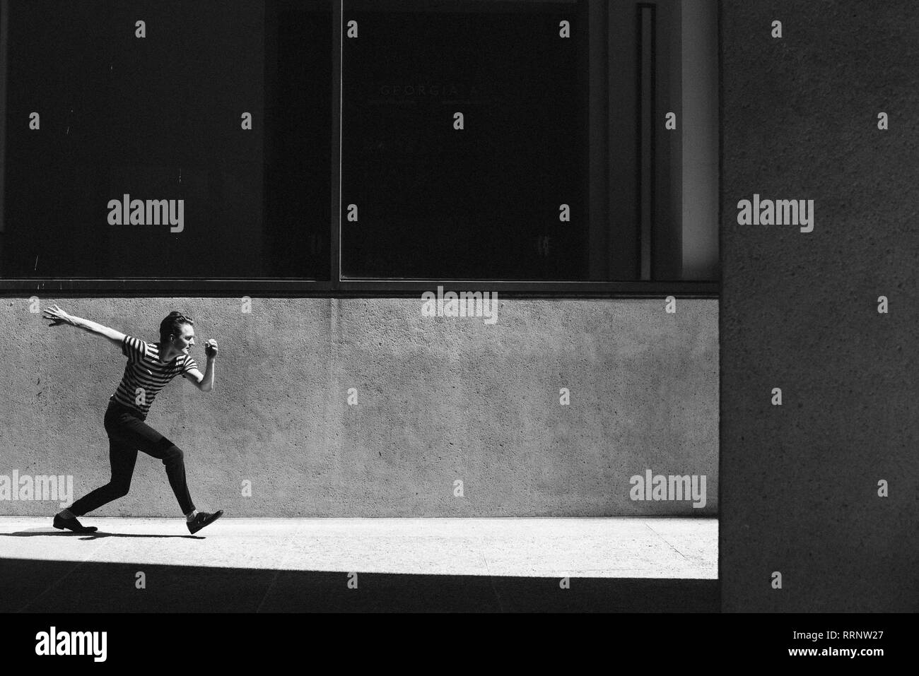 Jeune homme marchant sur un trottoir urbain ensoleillé Banque D'Images