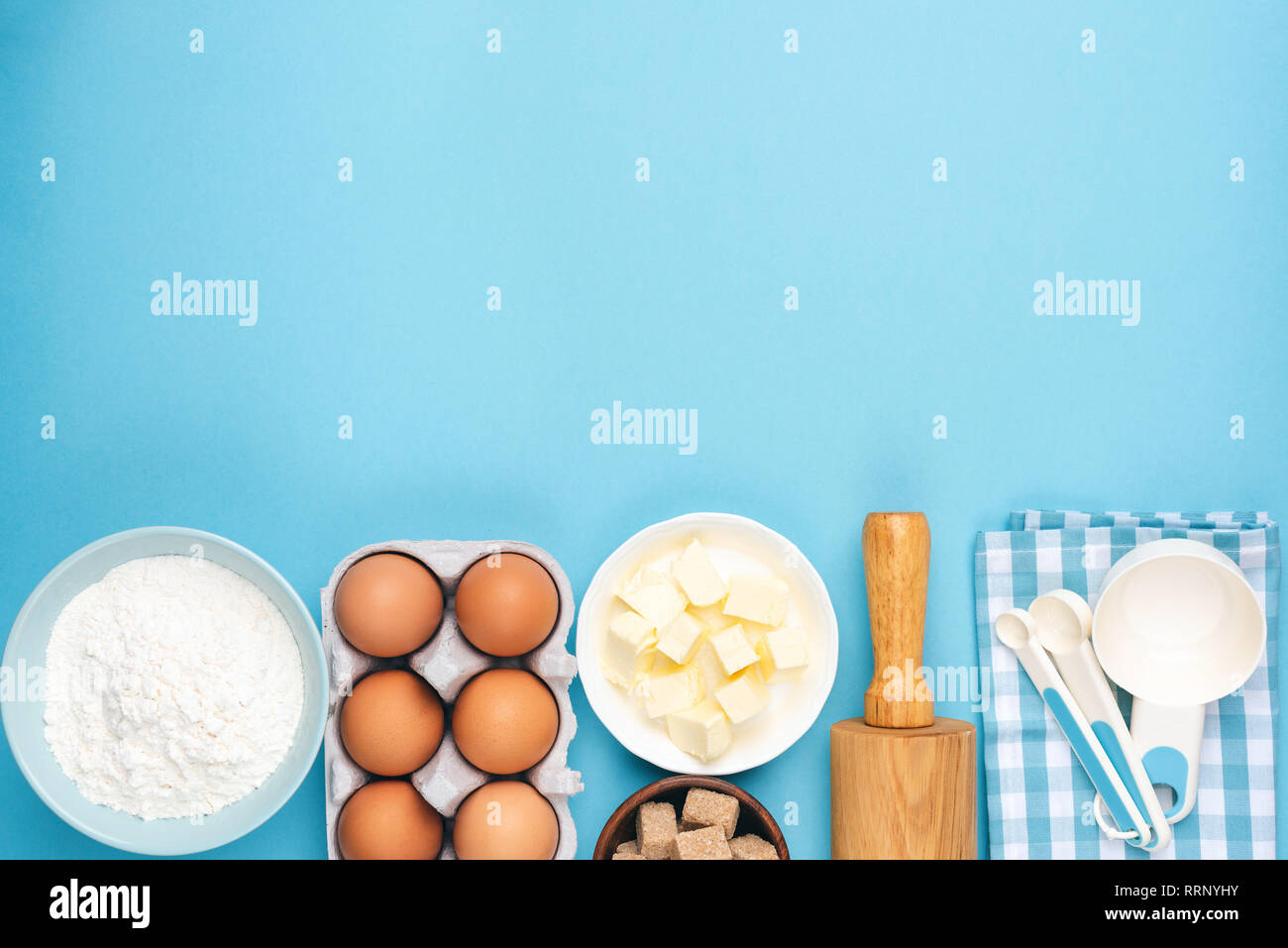 Ingrédients pour la cuisson ou la cuisson sur fond bleu. Les œufs, beurre, farine, cuillères à mesurer et de rouleau à pâtisserie. Pin up style rétro ou zone de nourriture de cuisine Banque D'Images
