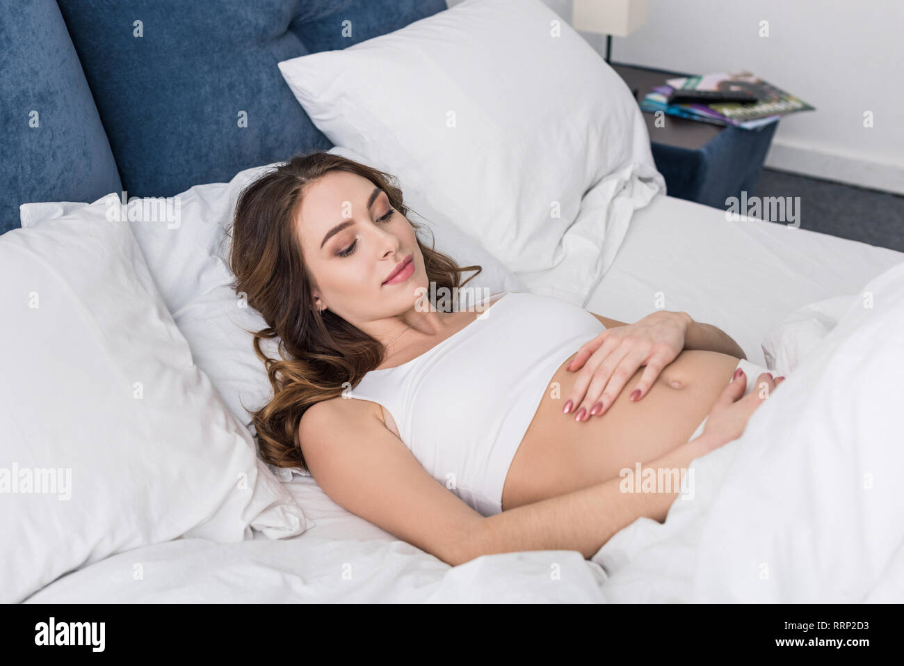 Charmante femme enceinte au lit et toucher ventre Banque D'Images