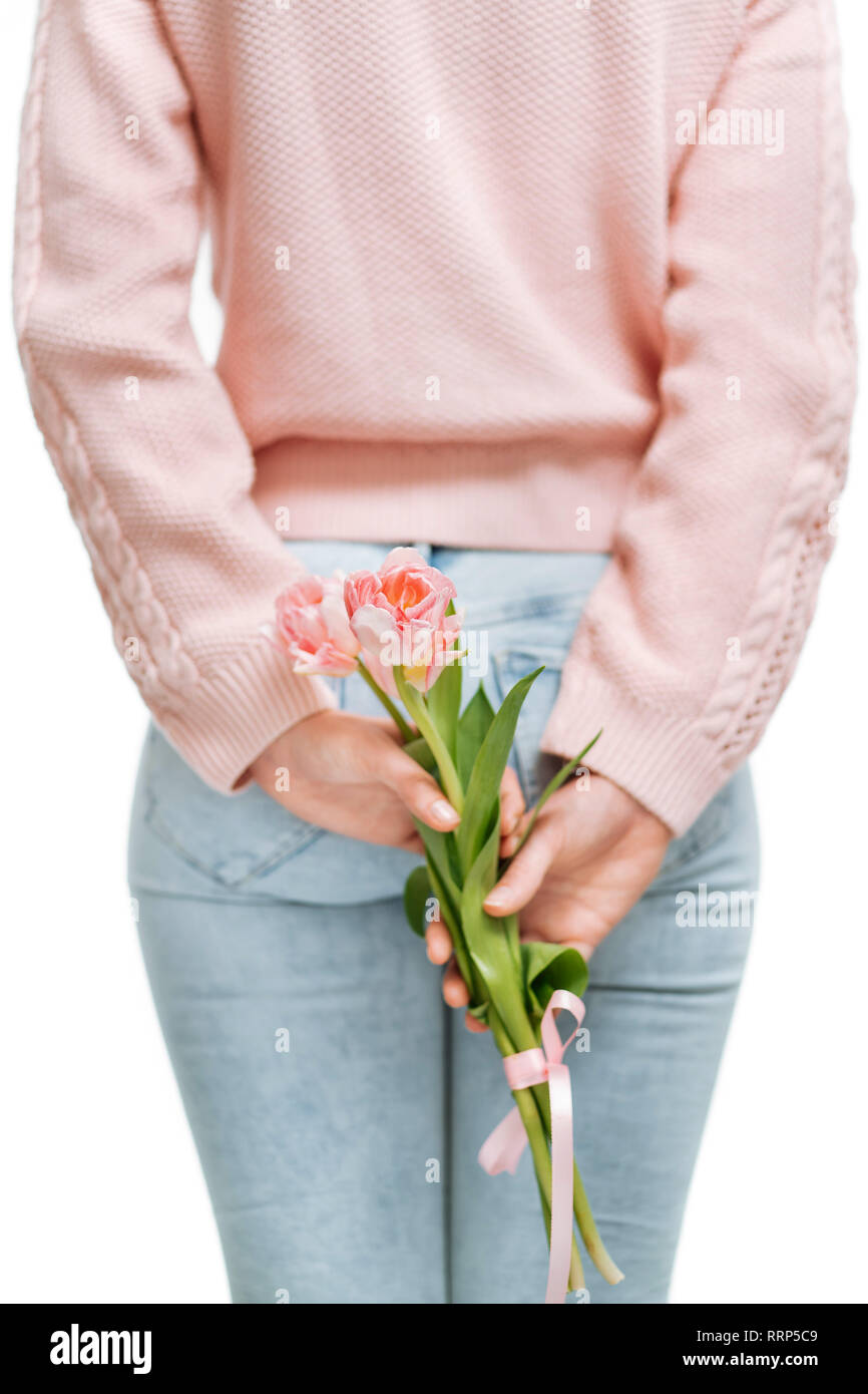 Jeune femme tenant de tulipes roses derrière son dos sur un fond blanc. Banque D'Images