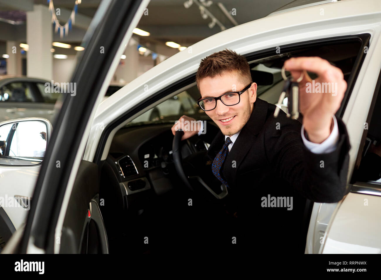 Smiling vendeur détient les clés de voiture en voiture. Banque D'Images