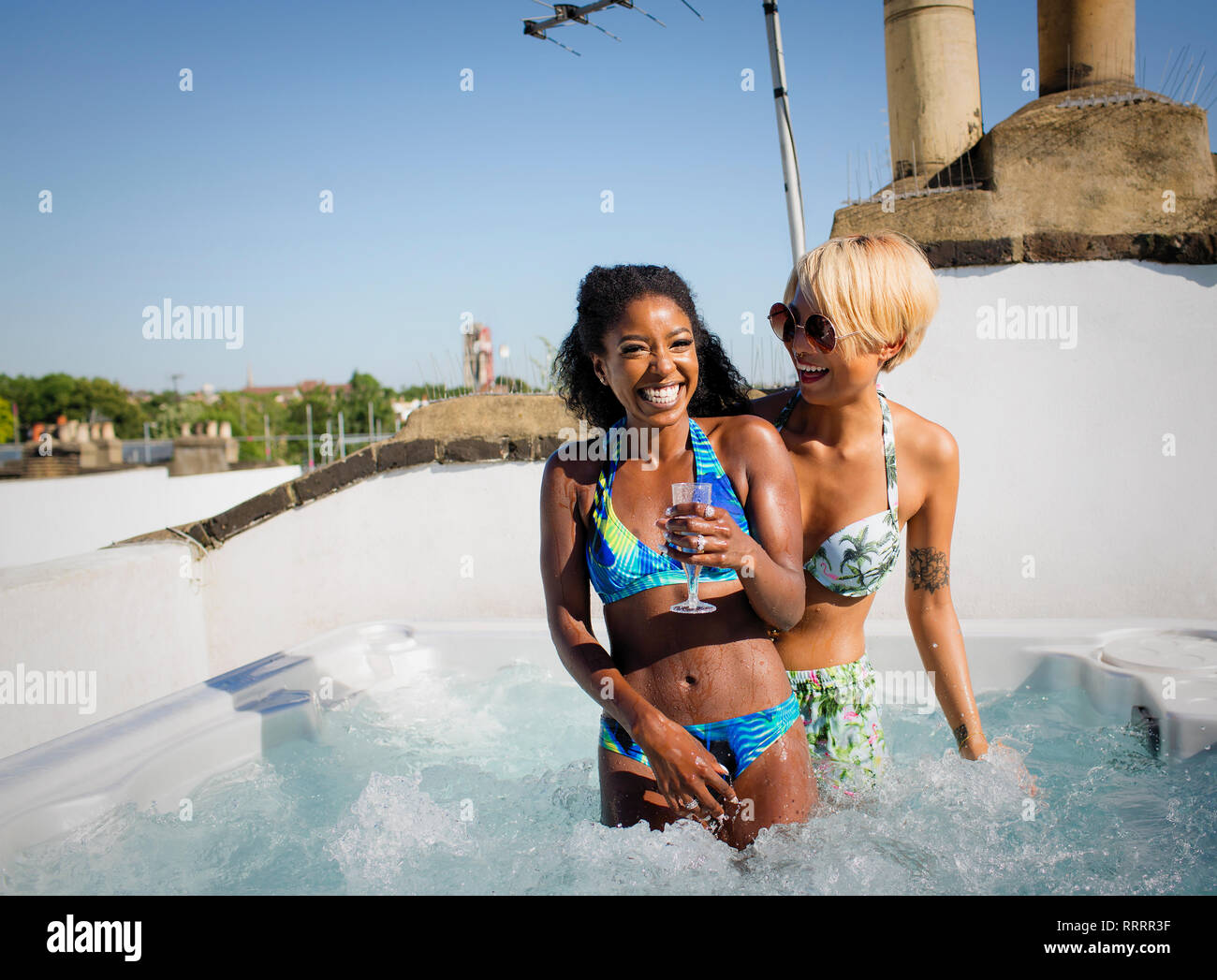 Portrait de rire, insouciant des jeunes femmes friends drinking champagne in sunny bain à remous sur le toit Banque D'Images