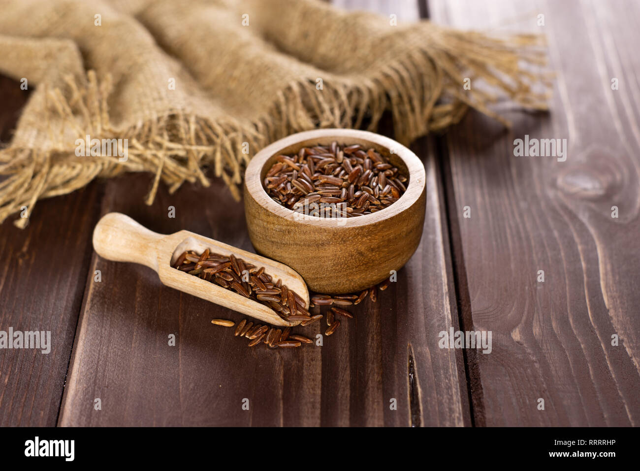 Beaucoup de riz rouge cru entier tissu du jute et d'un scoop avec bol en bois sur bois marron foncé Banque D'Images