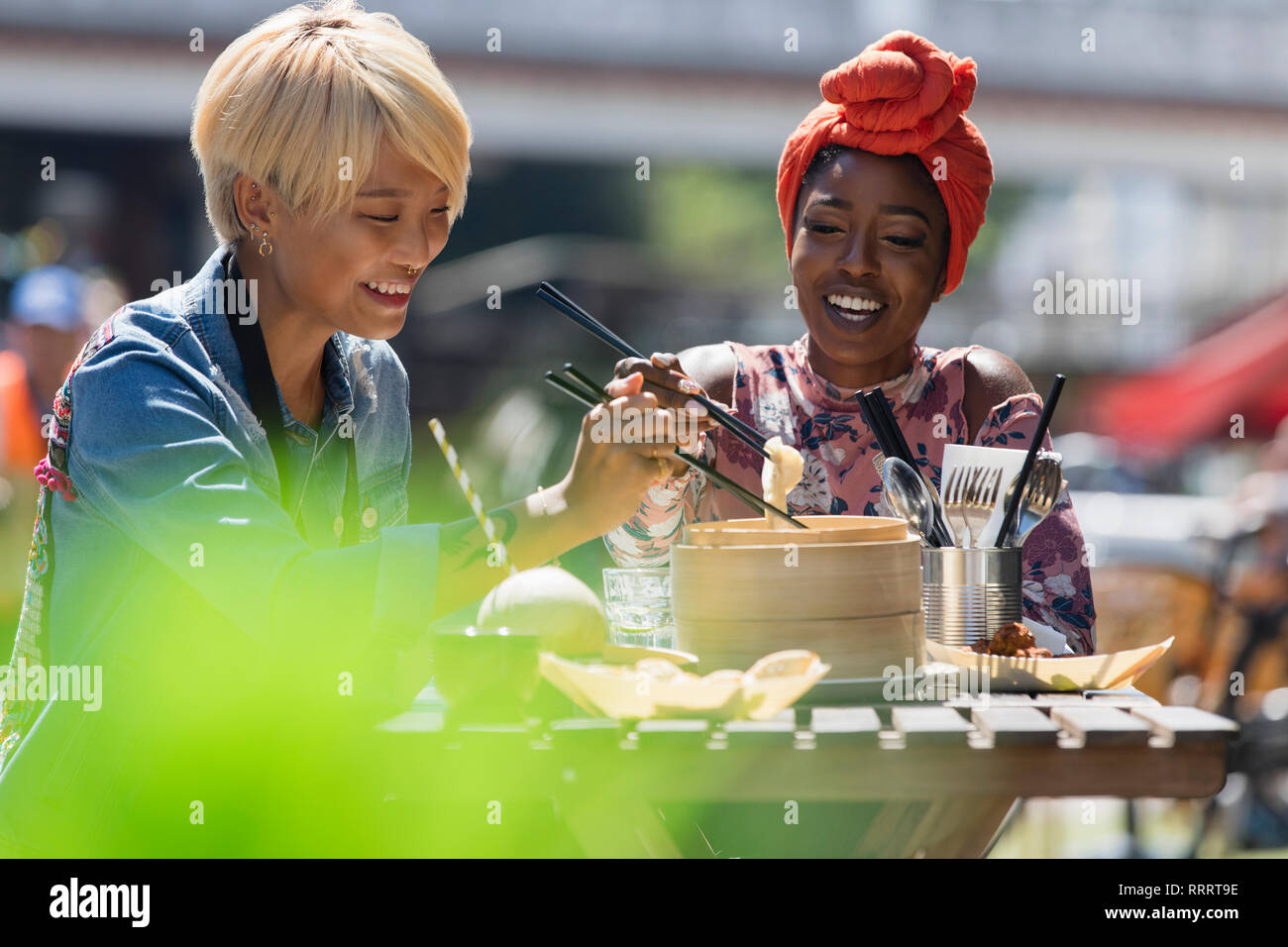 Les jeunes femmes bénéficiant d'amis déjeuner dim sum avec des baguettes au café avec terrasse ensoleillée Banque D'Images