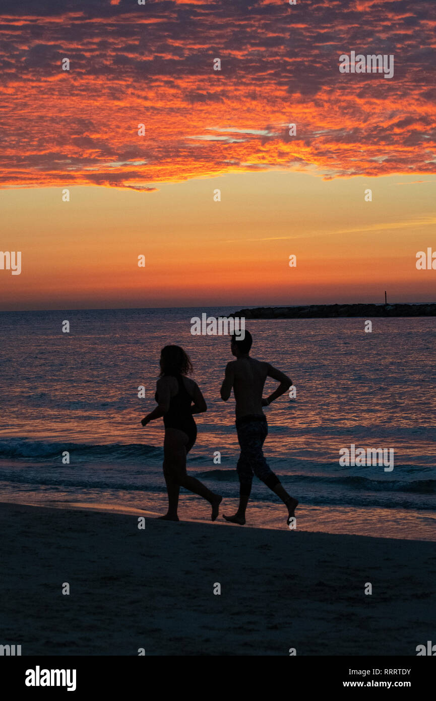 Un couple d'exécution sur la plage au coucher du soleil, la Tayelet de Tel Aviv, Israël Banque D'Images