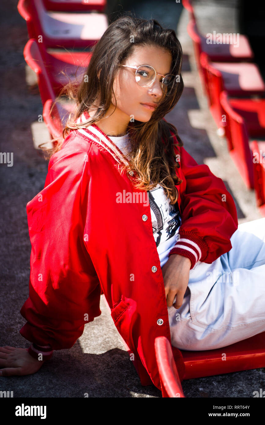 Jeune fille tennager modele dans le siege d un stade de baseball portant blouson rouge verres arrondis hipster un pantalon blanc et des chaussures Photo Stock Alamy