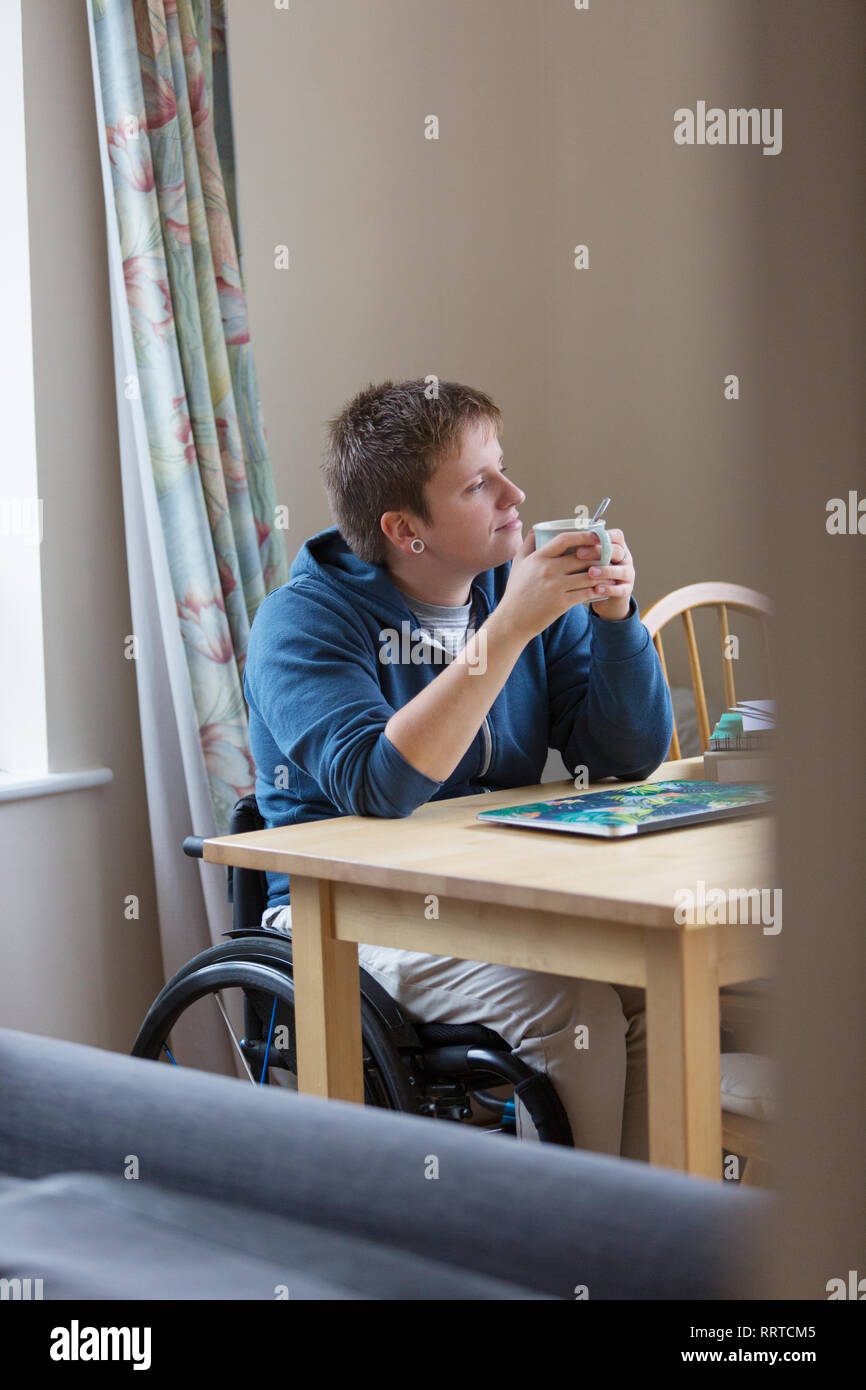 Young woman in wheelchair boire du thé à table à manger Banque D'Images