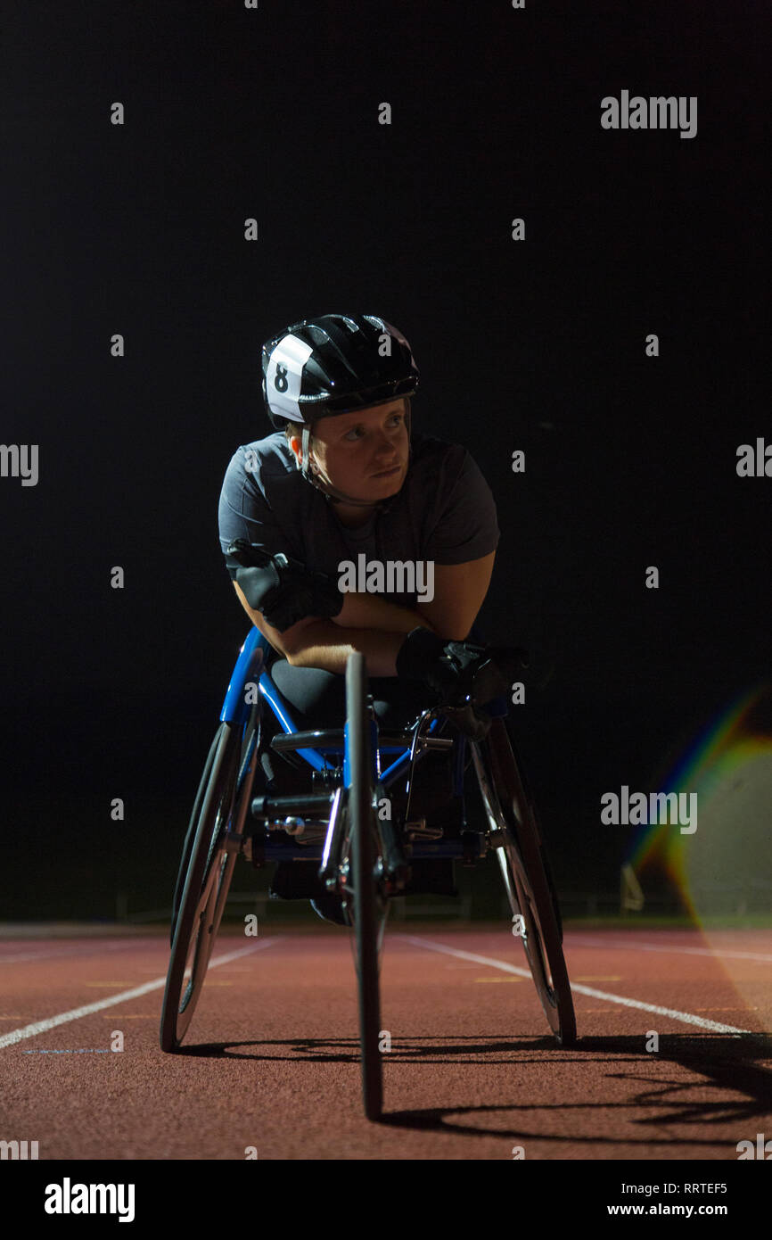 Jeune femme déterminée athlète paraplégique en fauteuil roulant pour la formation sur piste de course sports la nuit Banque D'Images
