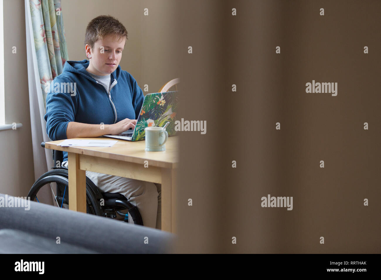 Jeune femme en fauteuil roulant à l'aide d'ordinateur portable à la table à manger Banque D'Images