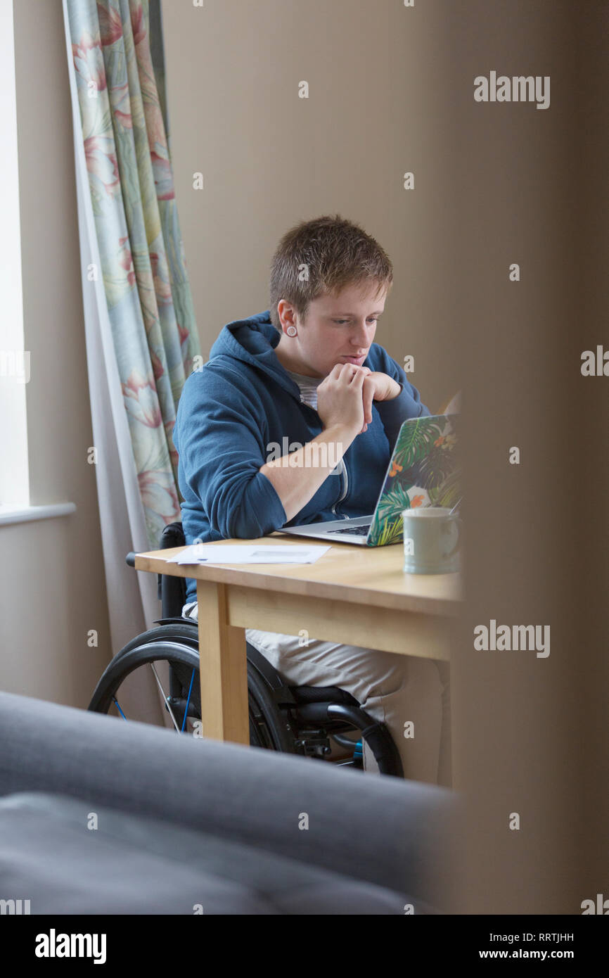 L'accent jeune femme en fauteuil roulant à l'aide d'ordinateur portable à la table à manger Banque D'Images
