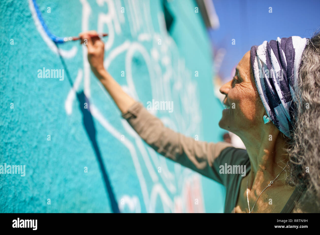 Senior woman painting peinture murale sur mur ensoleillé Banque D'Images