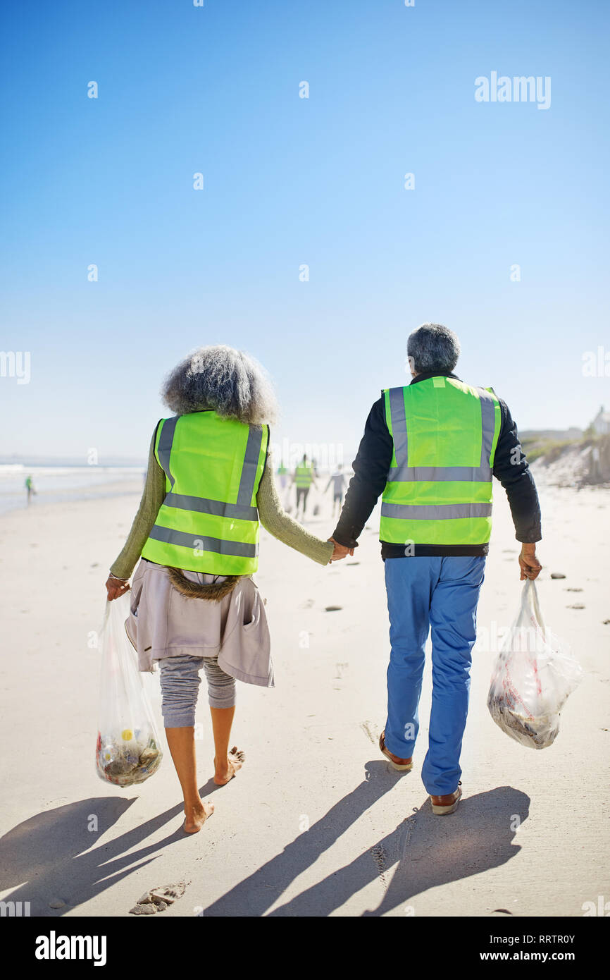 Romantic couple bénévoles nettoyage des déchets sur la plage de sable humide, ensoleillé Banque D'Images