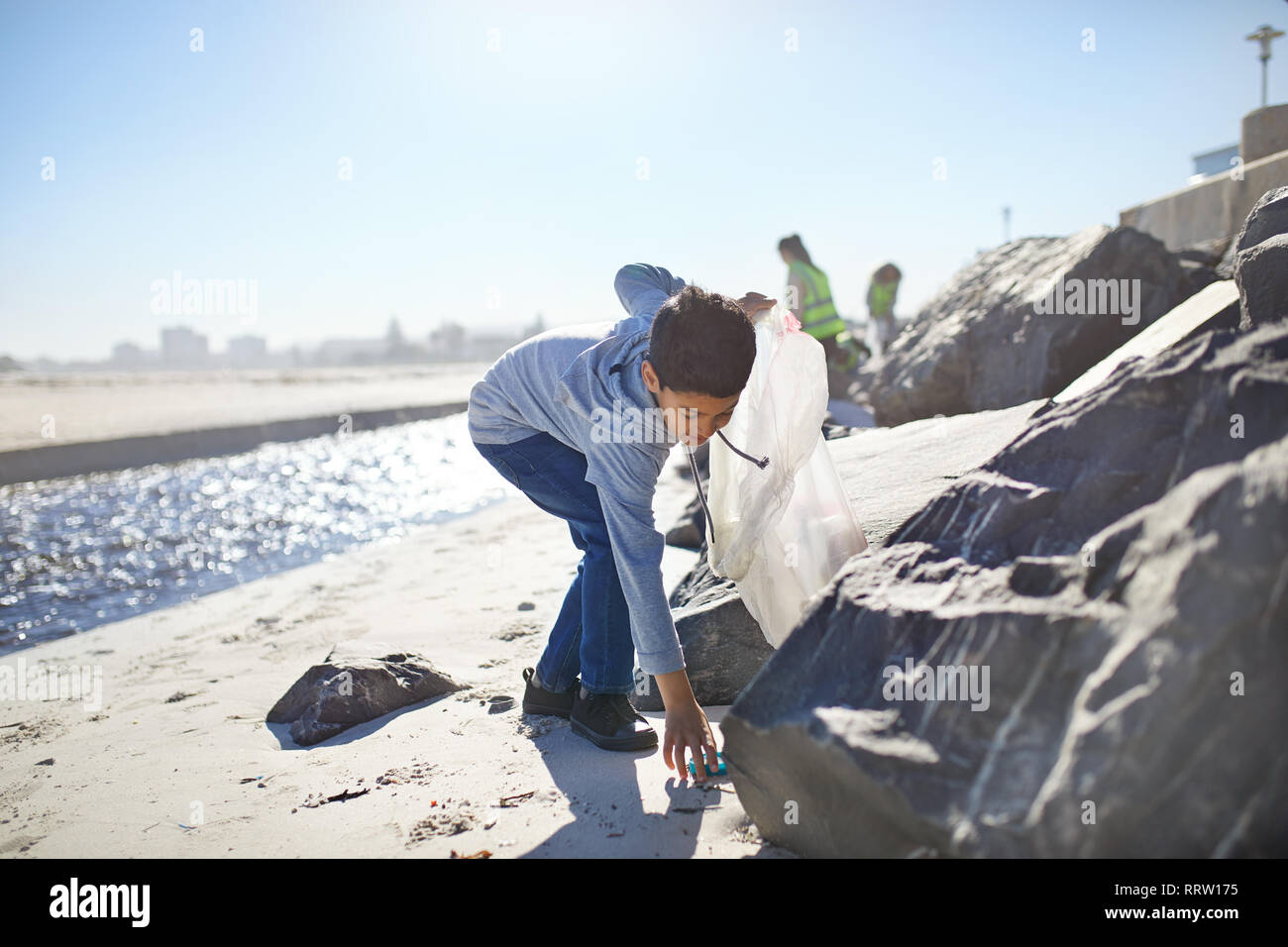 Bénévole garçon ramasser les déchets sur la plage ensoleillée Banque D'Images