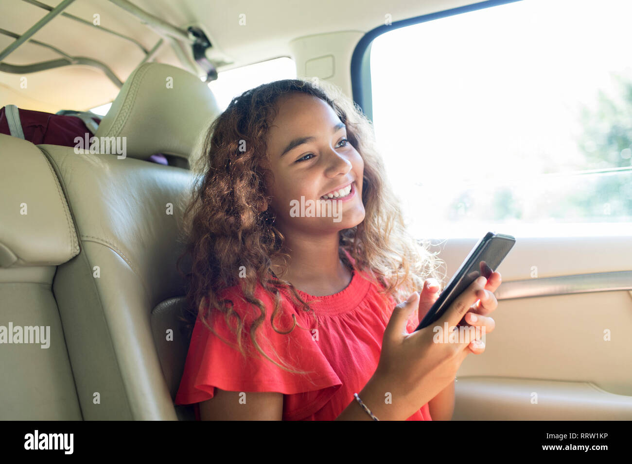 Tween Smiling girl using smart phone in back seat of car Banque D'Images