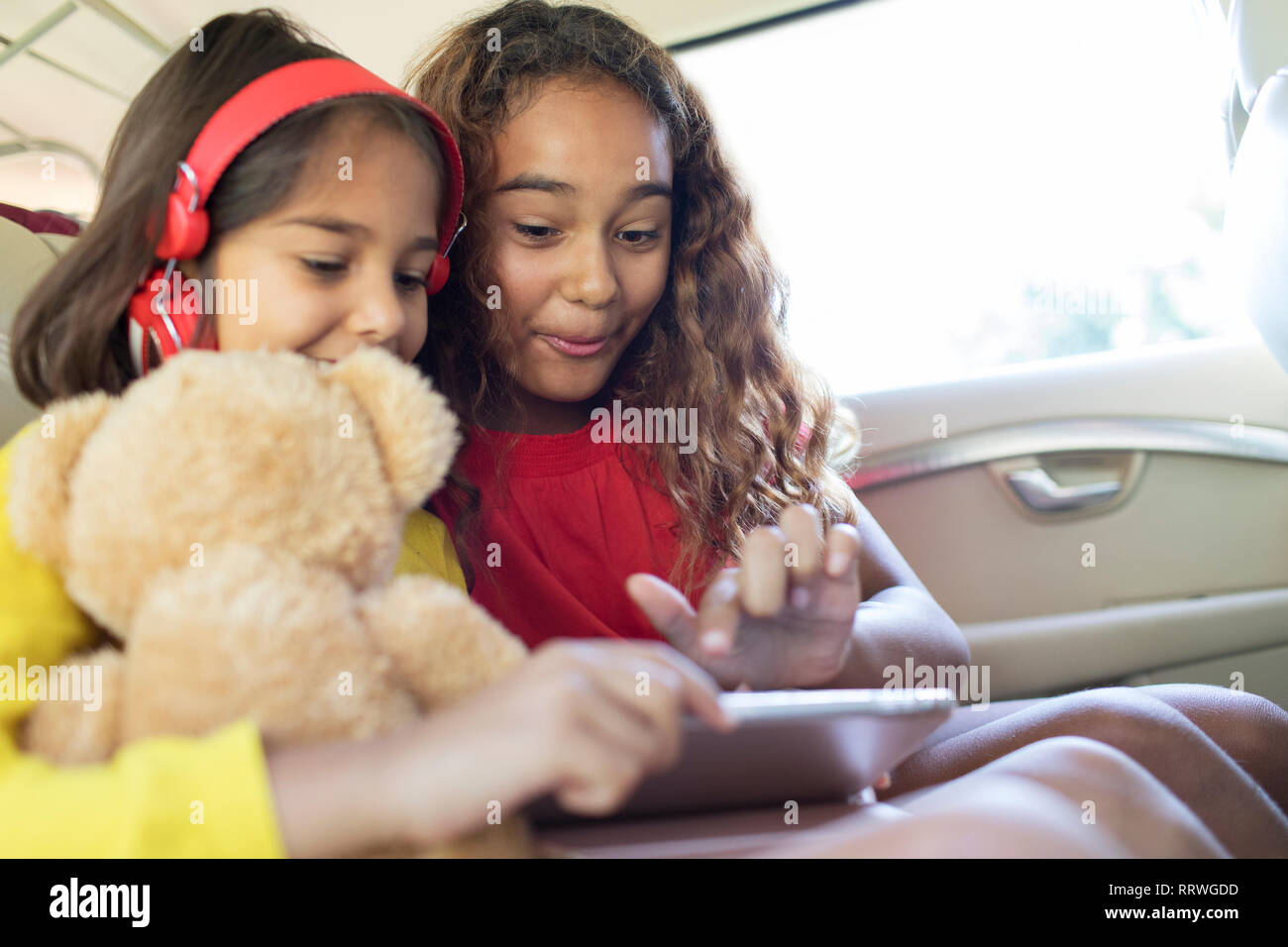 Sisters using digital tablet in back seat of car Banque D'Images