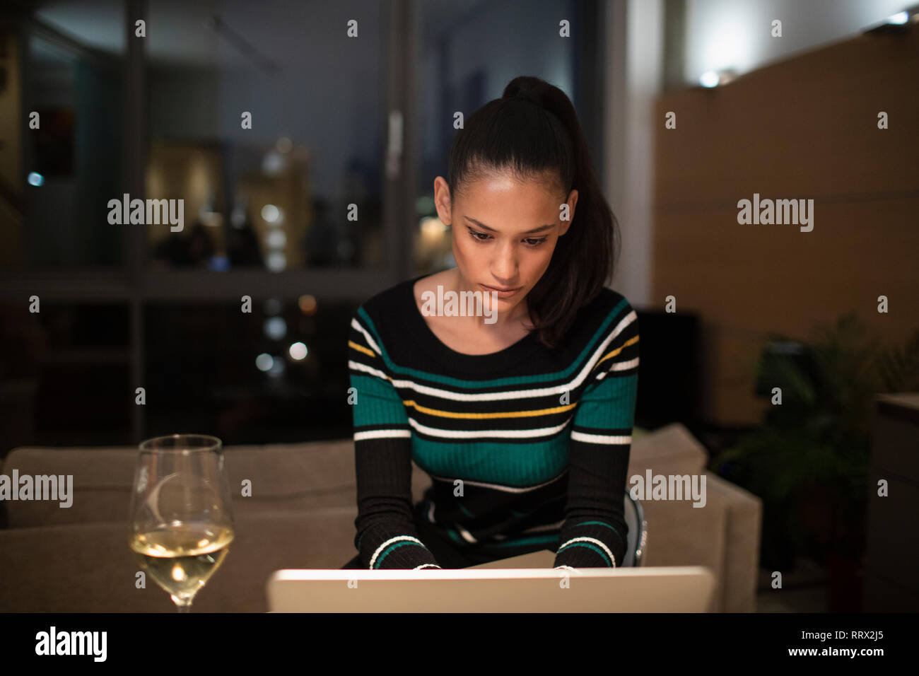 L'accent Femme buvant du vin blanc et de travail à l'ordinateur portable à la maison la nuit Banque D'Images