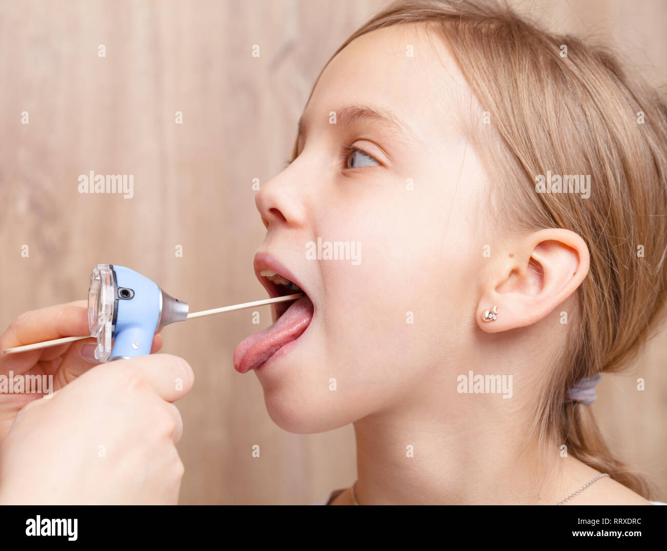 Pédiatre ou médecin examine la jeune fille d'âge élémentaire mal de gorge à l'aide d'abaisse-langue en bois et une lampe torche dans une clinique pédiatrique Banque D'Images