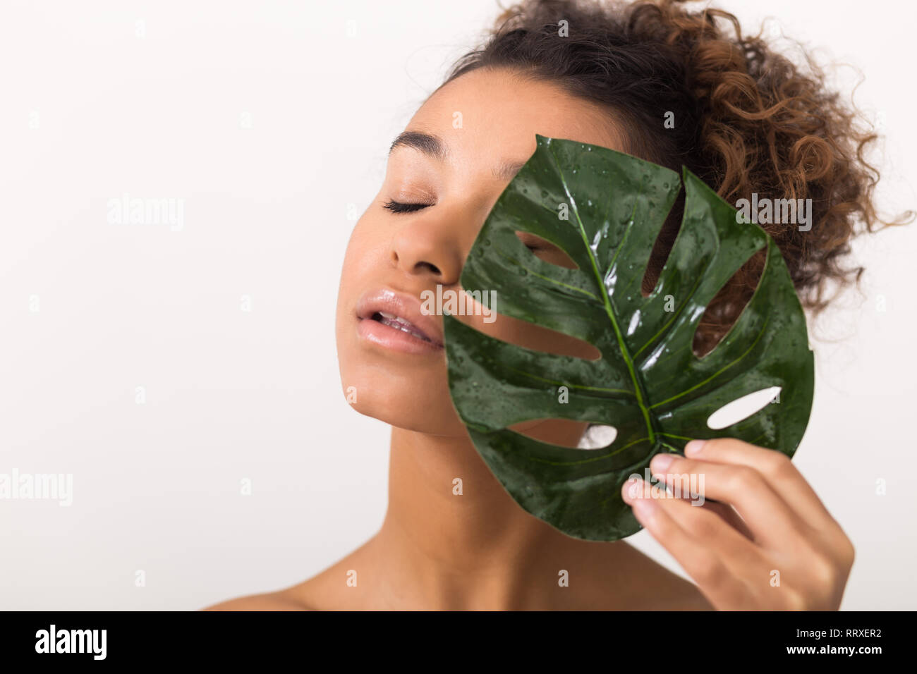 Fille avec des feuilles tropicales couvrant la moitié du visage Banque D'Images