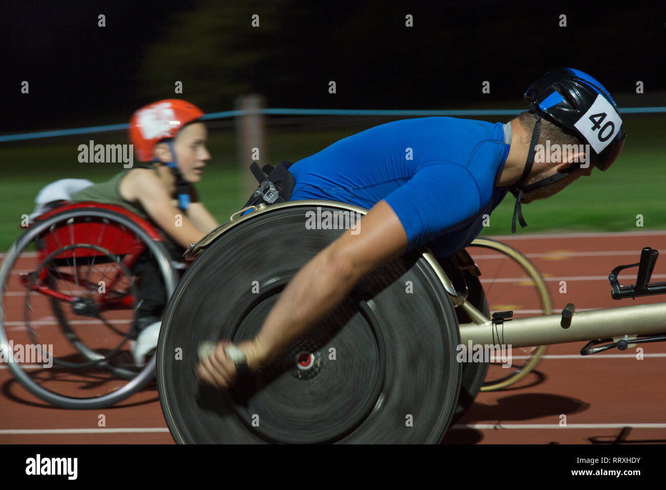 Les athlètes paraplégiques en accélérant le long de la voie des sports en fauteuil roulant de nuit course Banque D'Images