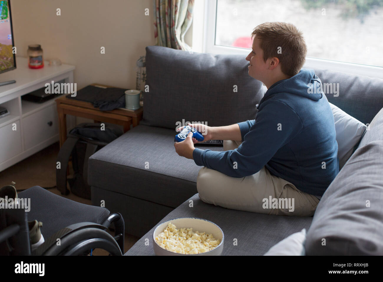 Young woman playing video game sur canapé à côté de fauteuil roulant Banque D'Images