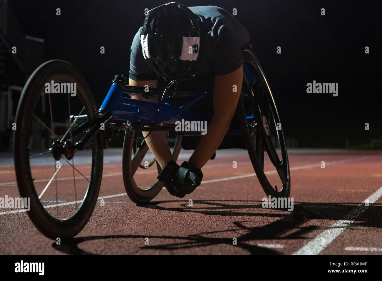 Fatigué athlète paraplégique reposant sur la piste après la course en fauteuil roulant sports at night Banque D'Images