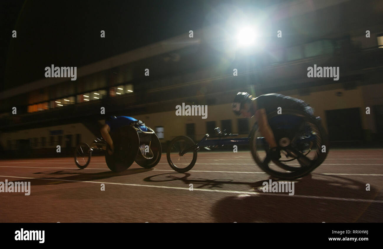 Les athlètes paraplégiques en accélérant le long de la voie des sports en fauteuil roulant de nuit course Banque D'Images