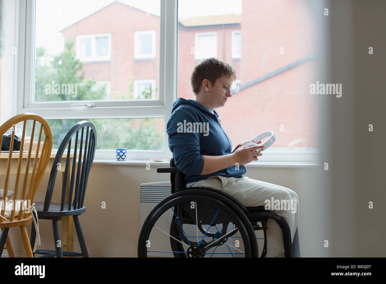 Jeune femme en fauteuil roulant avec des écouteurs à window Banque D'Images