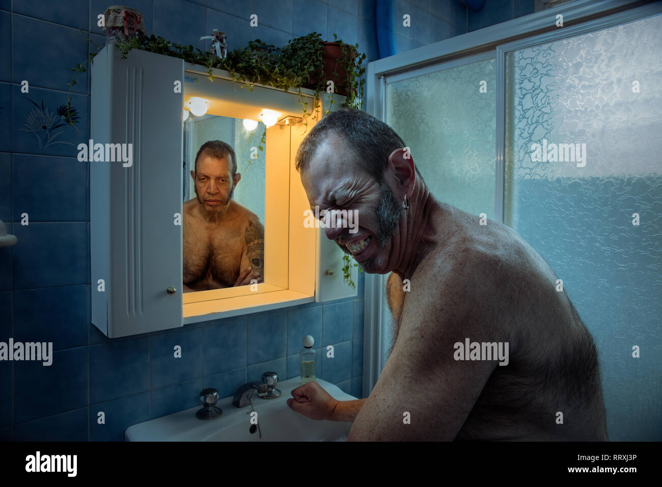 Homme mûr fronçant à partir de la douleur et le stress tout en se tenant  dans une salle de bains privative avec miroir de la réflexion à la  dépression Photo Stock -