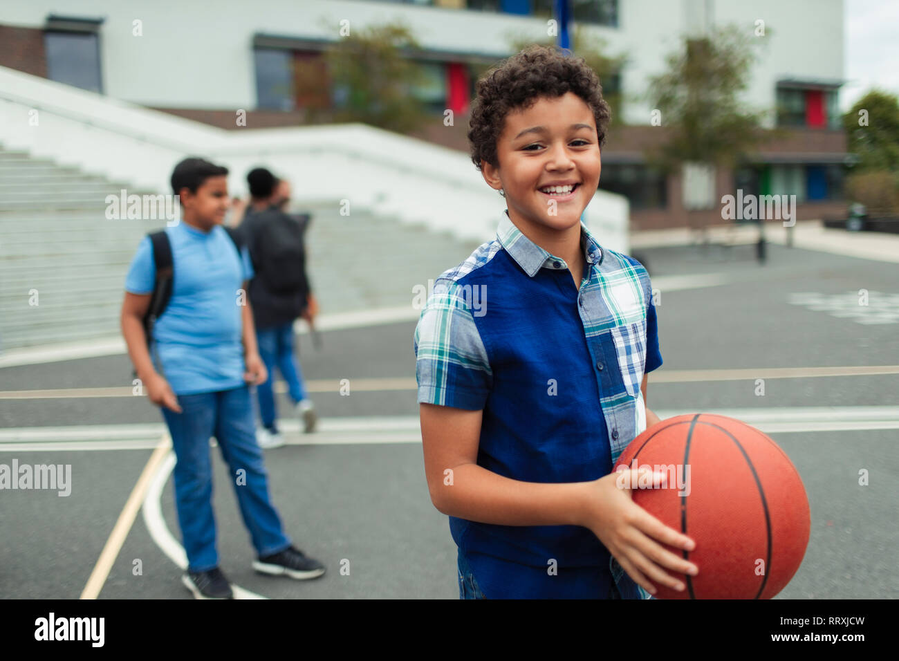 Portrait souriant, confiant le tween Garçon jouant au basket-ball dans la cour de l'école Banque D'Images