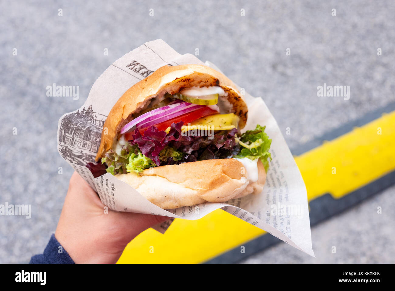 Main d'un jeune homme tenant un burger végétalien biologique avec le seitan patty dans sa main lors d'un festival de l'alimentation de rue Banque D'Images