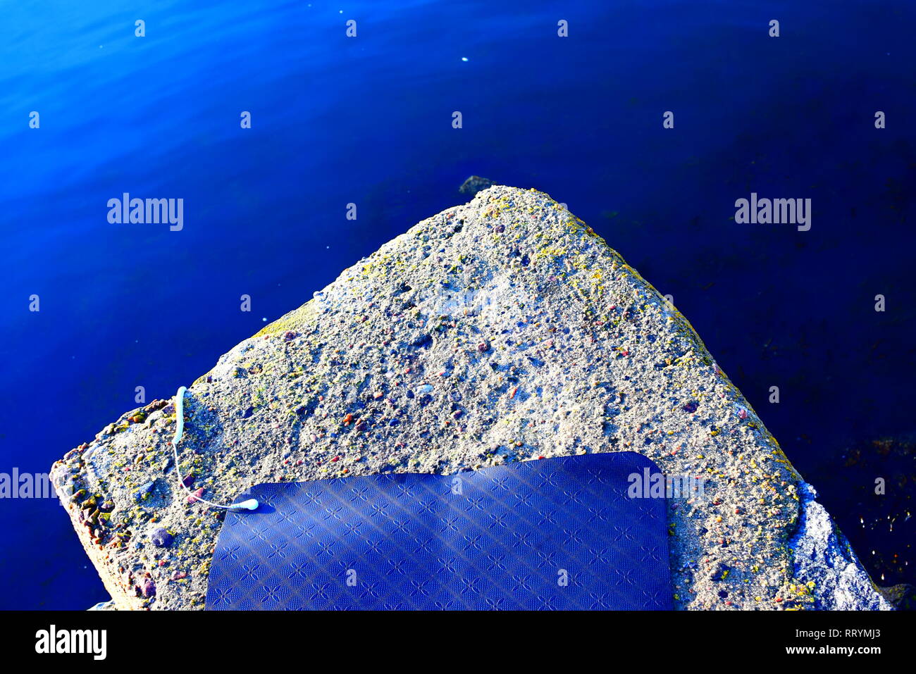 Le nouveau tapis de yoga à la terre noire avec des motifs dans le caoutchouc, tourné pendant une forte lumière du soleil à la plage par la mer Banque D'Images