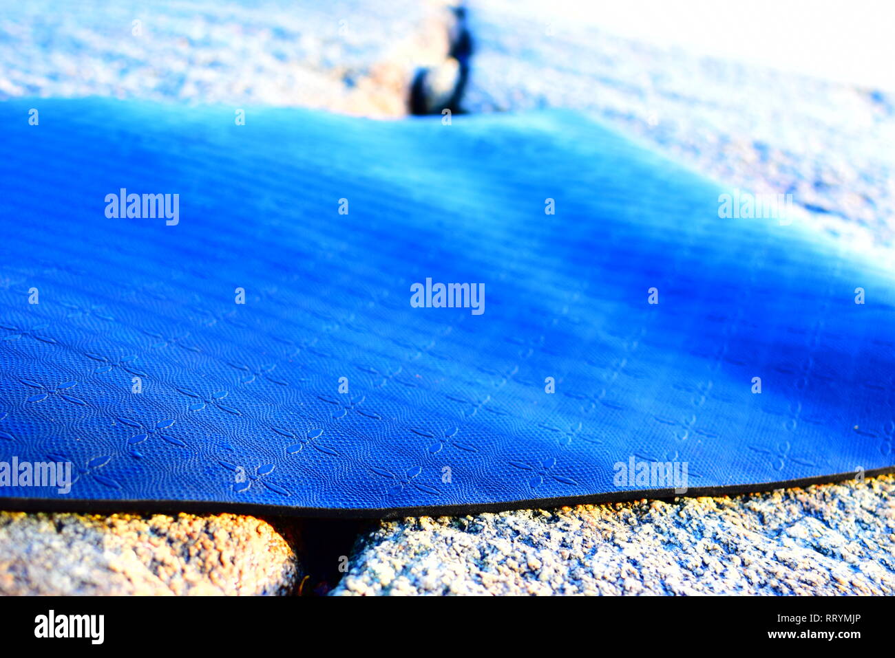 Le nouveau tapis de yoga à la terre noire avec des motifs dans le caoutchouc, tourné pendant une forte lumière du soleil à la plage par la mer Banque D'Images