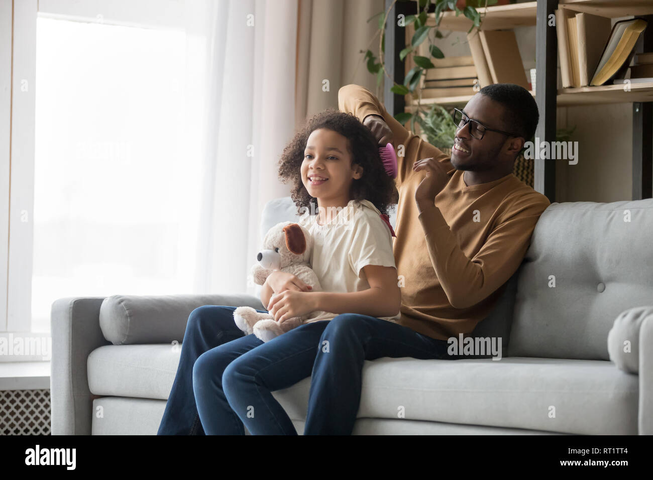 Brossage des cheveux africains papa faisant de daughter sitting on sofa Banque D'Images