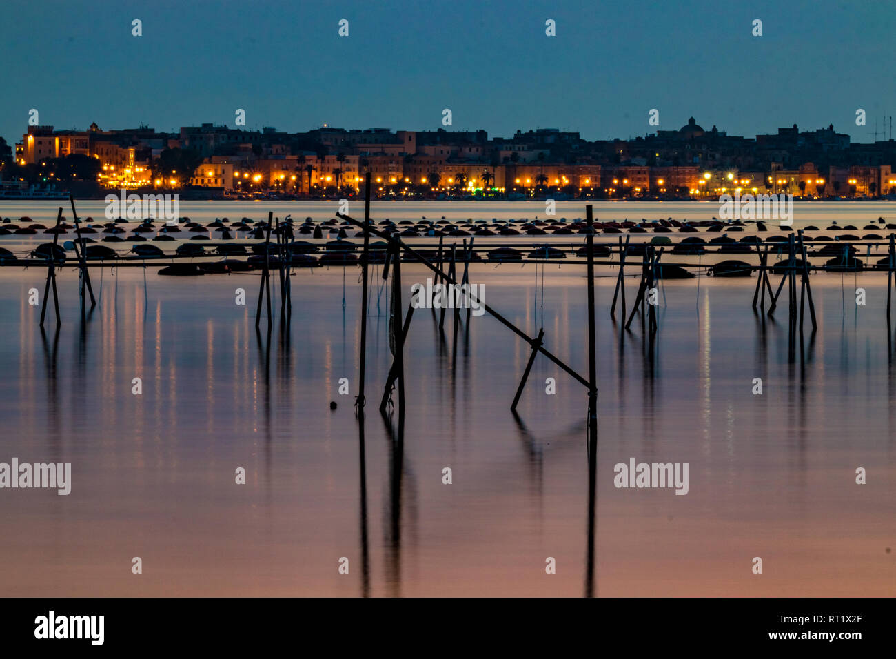 La photographie de nuit, longue exposition libre du chantier naval et de la zone industrielle à Taranto, Italie avec du matériel de pêche dans l'avant et de belles réflexions de l'eau et le coucher du soleil couleurs Banque D'Images