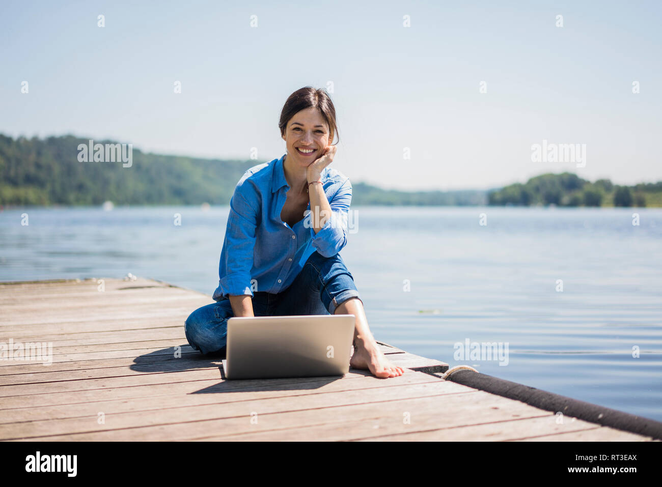 Femme mature de travailler à un lac, à l'aide de l'ordinateur portable sur une jetée Banque D'Images