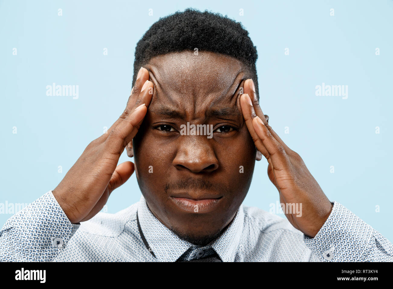 L'homme ayant des maux de tête. Isolé sur fond bleu. L'african businessman standing avec douleur isolé sur fond bleu à la mode studio. La moitié des hommes portrait en pied. Les émotions humaines, l'expression faciale concept. Banque D'Images