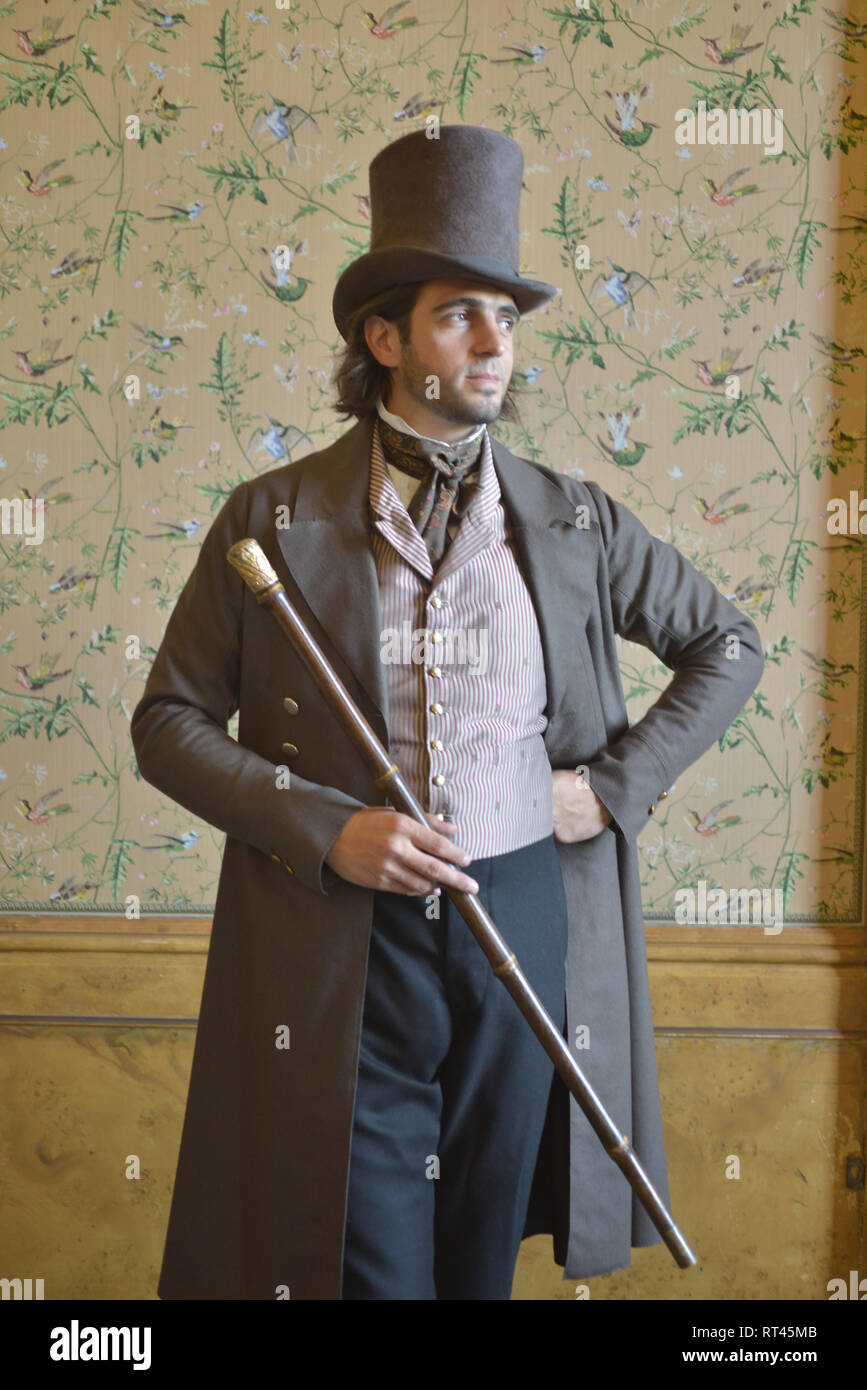 Un beau jeune homme de l'époque victorienne dans un costume historique se  dresse contre une toile de fond d'un portrait- il a un haut de forme et  canne à sucre Photo Stock -