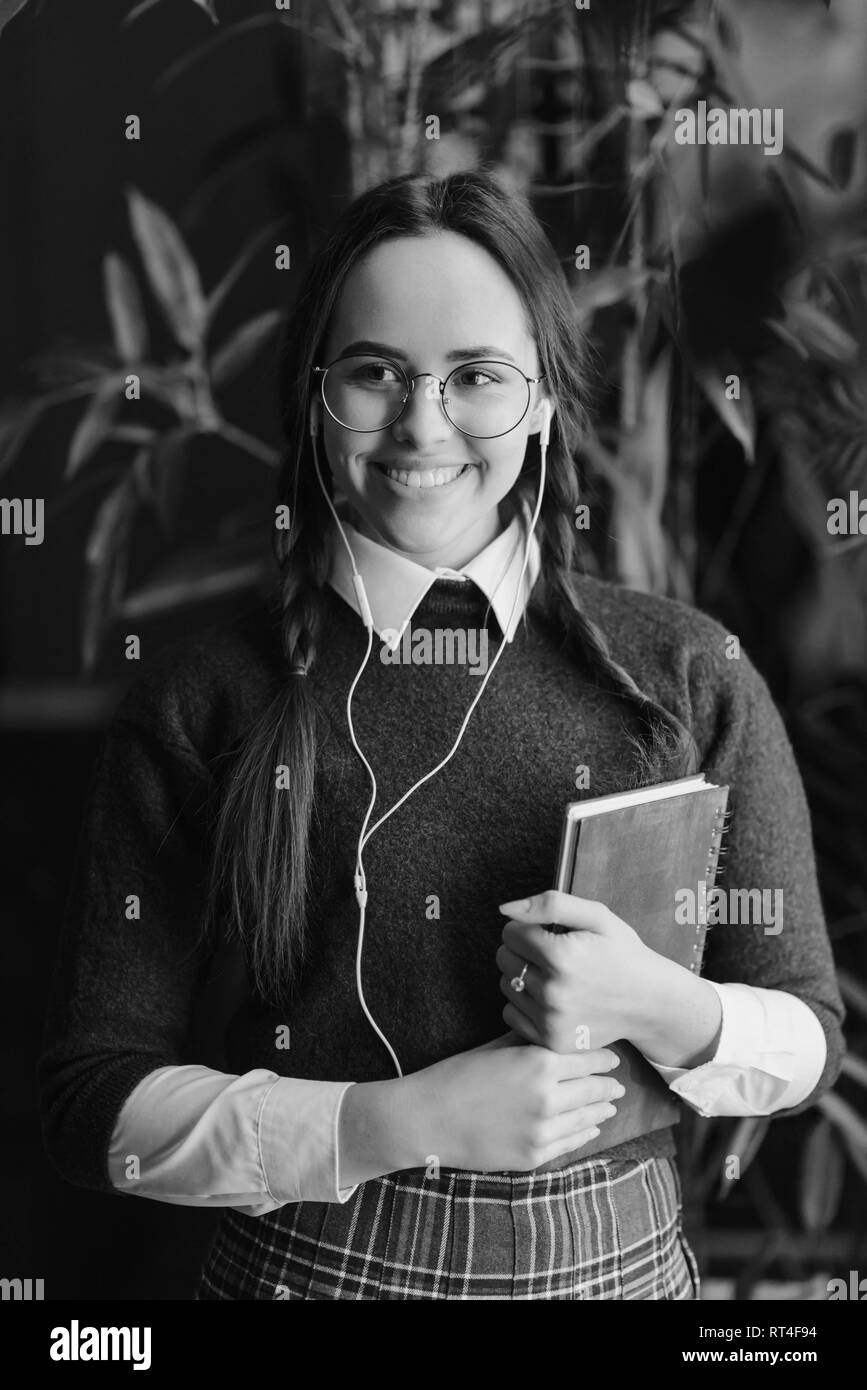 Fille brune avec des tresses en verres en uniforme avec un ordinateur portable debout près de la fenêtre et écouter la musique Banque D'Images