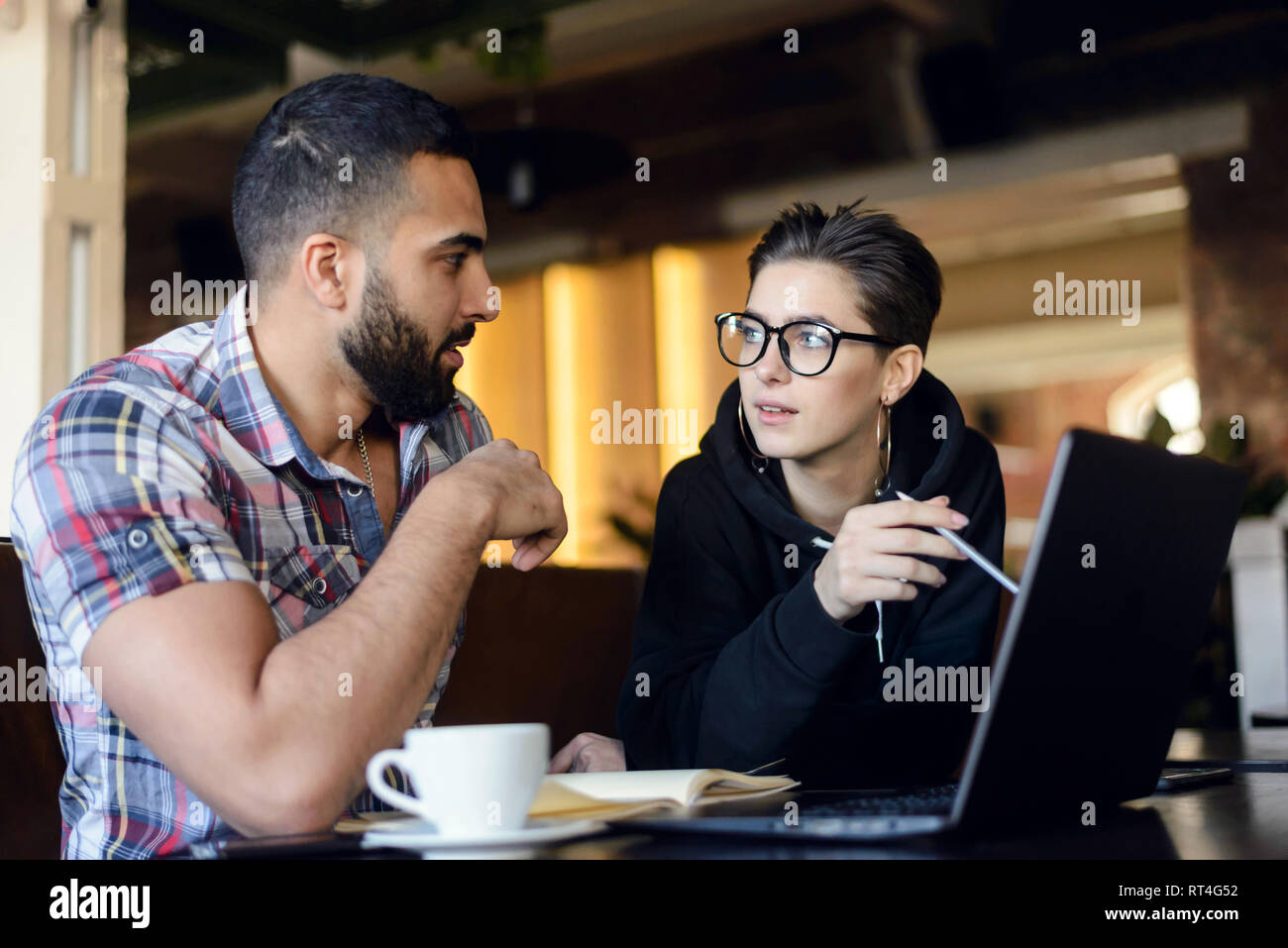 Deux camarades astucieux d'avoir une conversation amicale tout en faisant ses devoirs avec l'ordinateur portable à l'intérieur cafe Banque D'Images